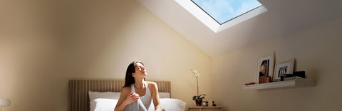 Woman sitting on a bed in a room with a skylight, smiling.